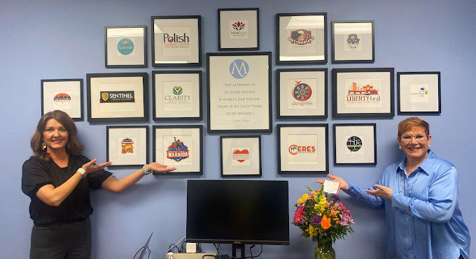 Aundrea and Agi in the Marquee office standing in front of Marquee-designed logos